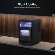 Black ice maker with transparent window on a kitchen counter, featuring night lighting and timer function.